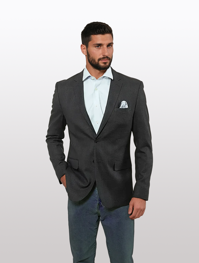 A man in a Fubu The Colle Black Windowpane Slim Fit Sport Jacket and light blue shirt stands confidently with one hand in his pocket against a plain background.
