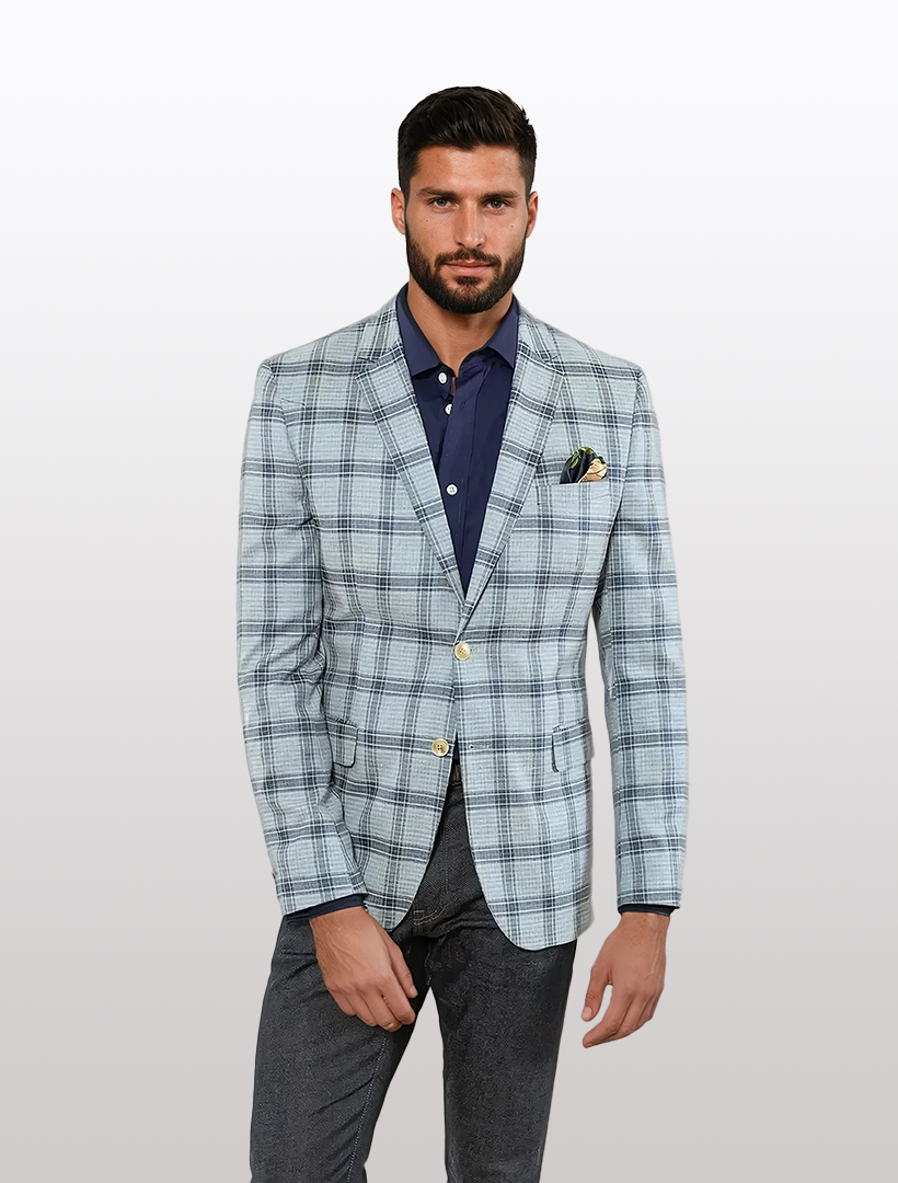 A man in a FUBU light blue with dark blue windowpane slim fit sport jacket, styled with a navy shirt and dark pants, stands with one hand in his pocket against a plain background.