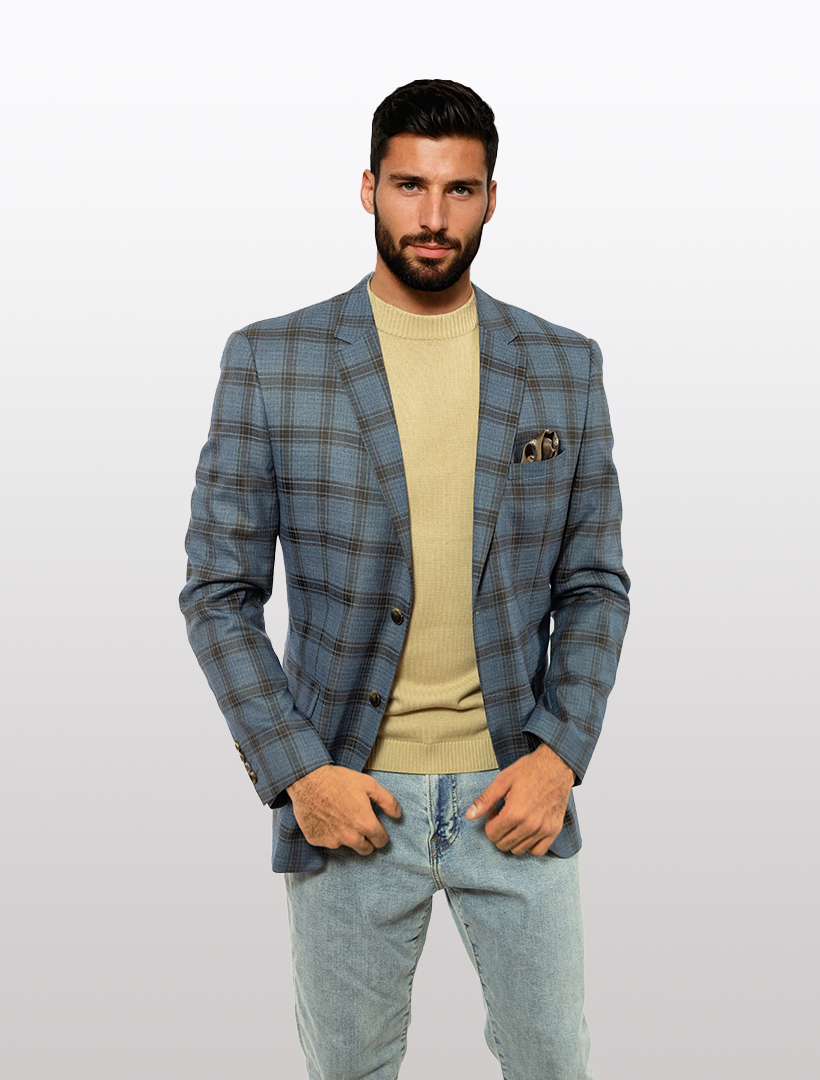 A man in a FUBU Blue with Brown Windowpane Slim Fit Sport Jacket by Fubu The Colle, beige sweater, and light jeans stands against a plain background.