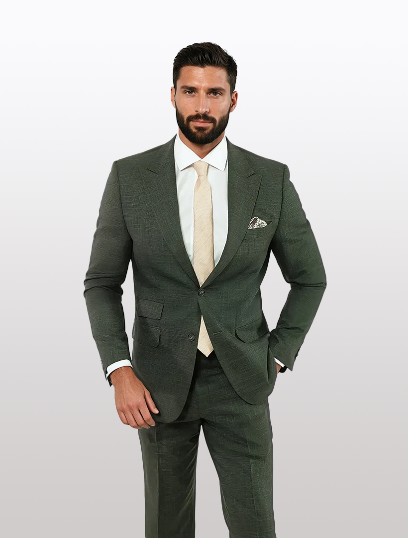A man in a FUBU Olive Green Peak Lapel 2-Piece Suit by Fubu The Colle, paired with a beige tie and pocket square, stands against a light gray background.