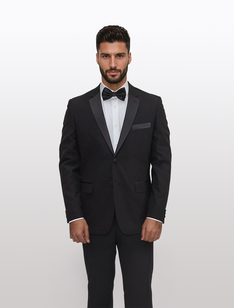 A man in a FUBU Classic Notch Lapel Black Tuxedo by Fubu The Colle stands against a plain white background, his bow tie completing the sophisticated look.