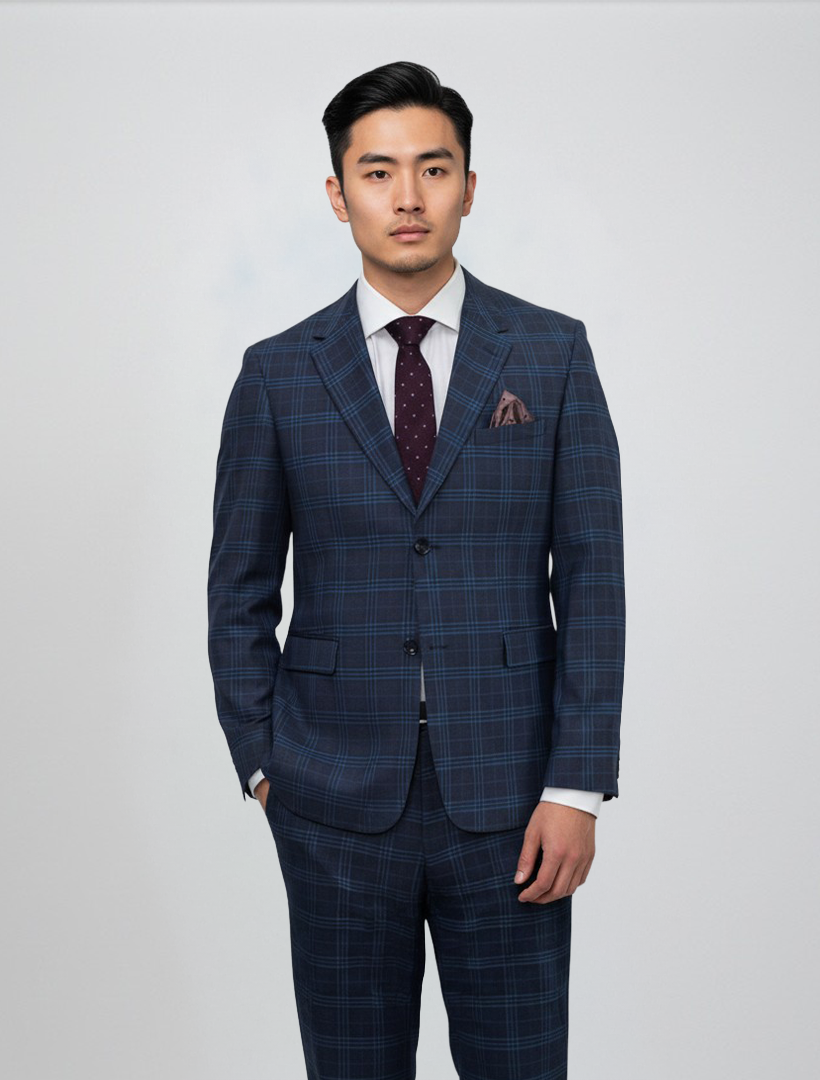 A man is wearing the Gianco Ferro Men’s Charcoal with Navy Pattern Slim Fit Suit, featuring a premium Tetron Rayon construction and stretch armhole design for enhanced comfort. The suit displays a refined blue plaid pattern and is styled with a crisp white shirt, burgundy polka dot tie, and coordinating pocket square, all set against a light gray background.