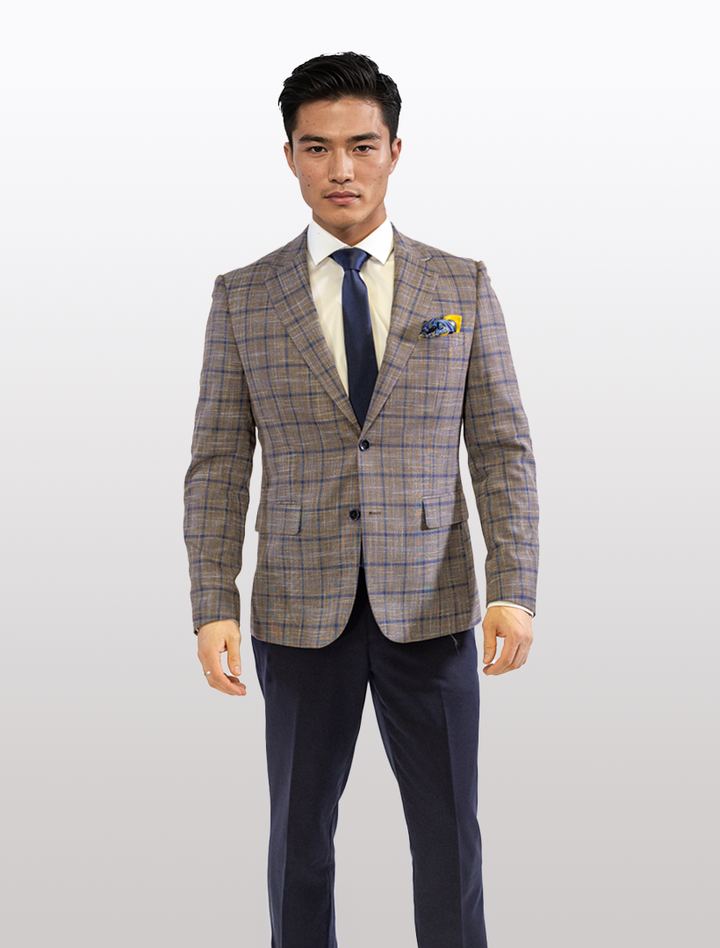 Man in a FUBU Cedar Brown with Royal Blue Windowpane Sport Jacket by Fubu The Colle, wearing a white shirt and navy tie, standing against a plain background.