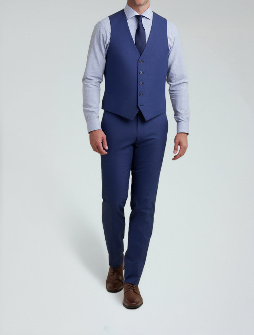 A person in the Allure Men's Royal Blue Tailored Fit Vest, paired with a blue suit, light blue shirt, blue tie, and brown dress shoes made from Tetron Rayon, stands against a plain light background.