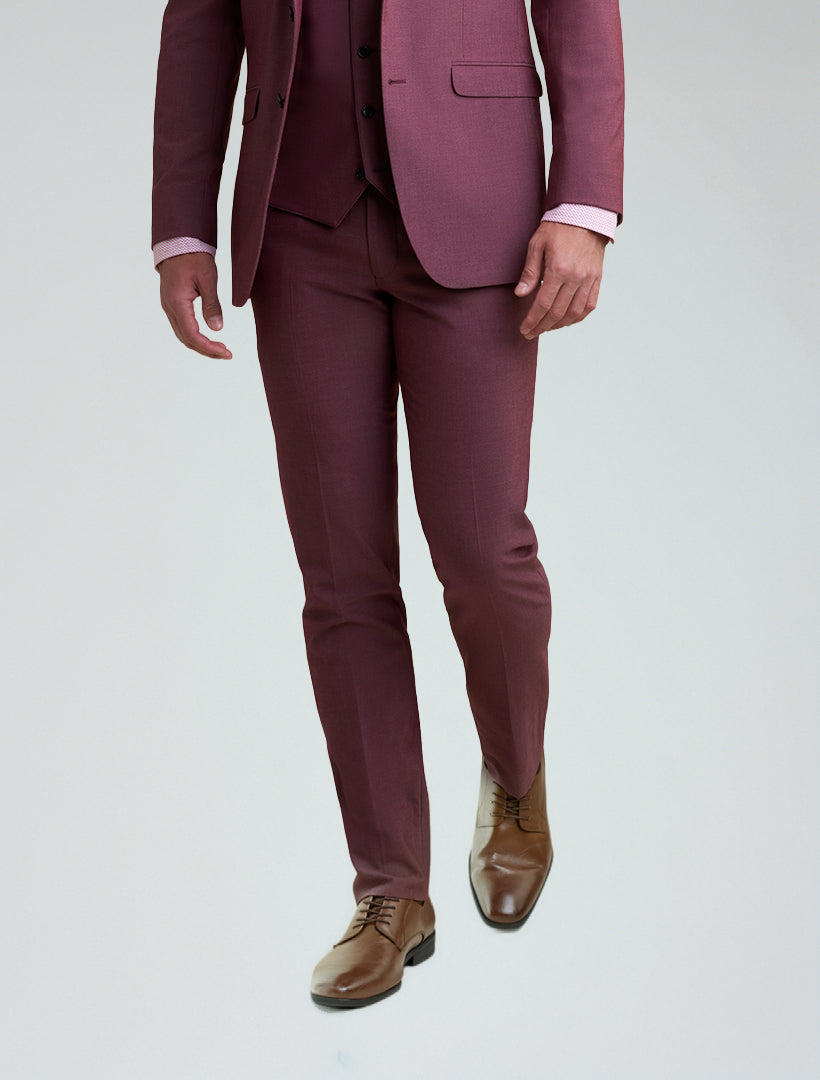 A man stands against a plain background wearing Allure's Men's Burgundy Tailored Fit Dress Pants, paired with a matching suit, light pink shirt, and brown dress shoes.