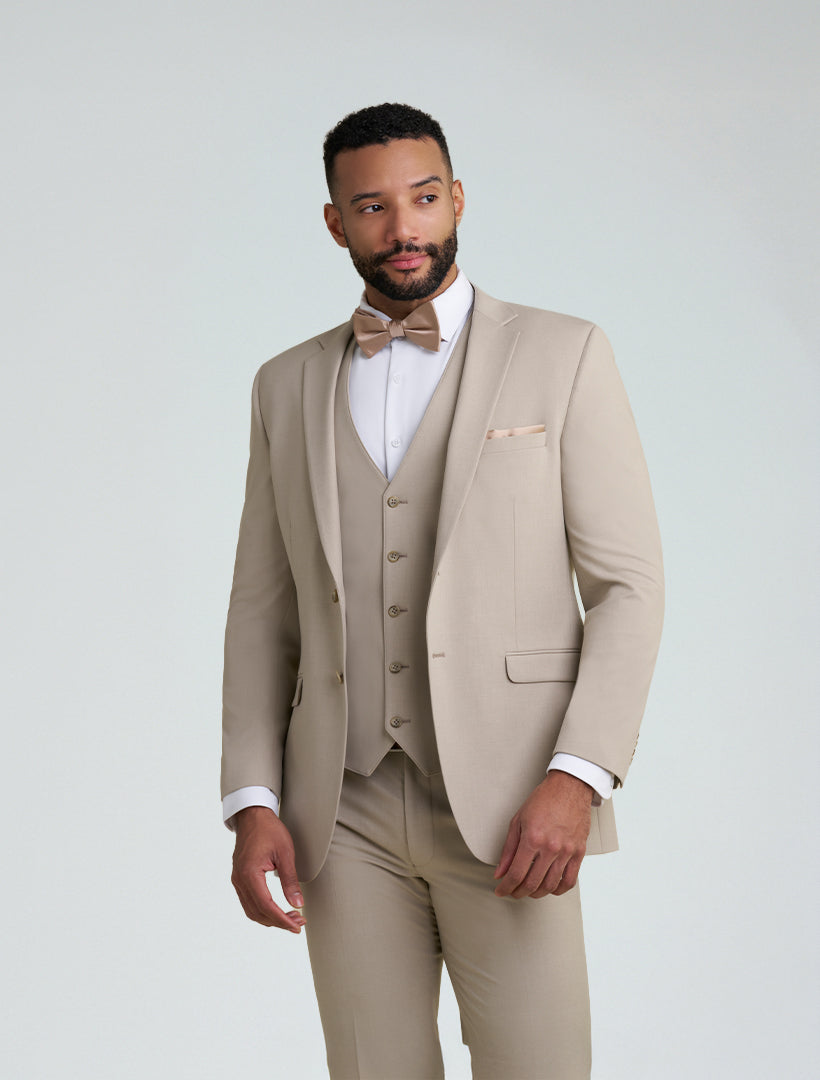 A man stands against a plain light background wearing the Allure Men's Tan Tailored Fit Suit Jacket with matching vest, bow tie, pocket square, and a white dress shirt.