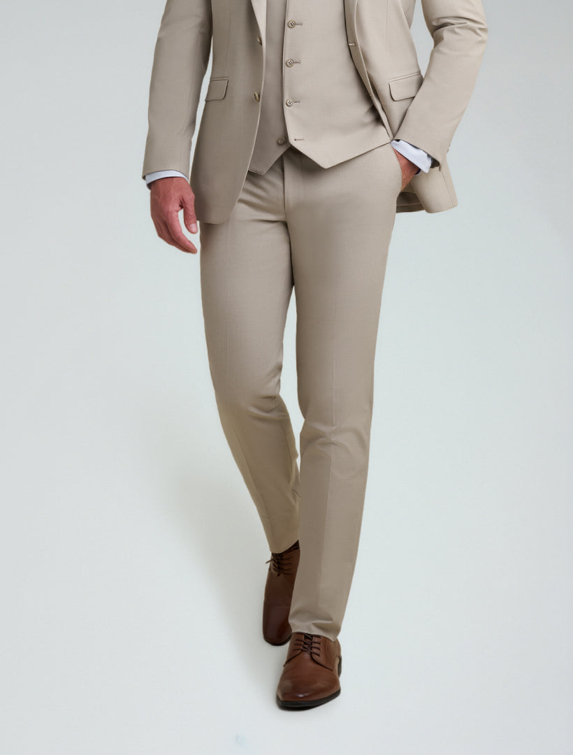 A person wearing Allure Men's Tan Tailored Fit Dress Pants, paired with a white shirt and brown dress shoes, walking on a plain light background.