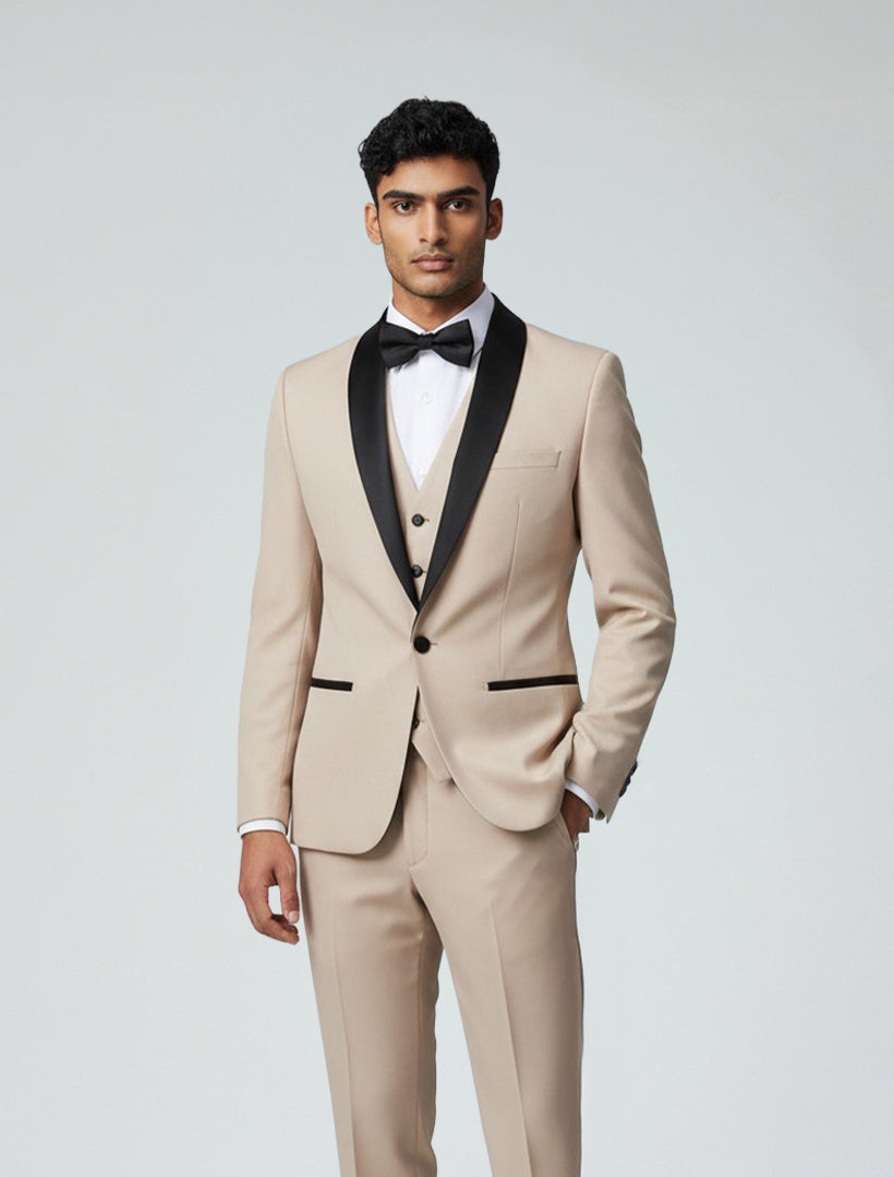 A man in a Gino Vitale Men's Beige Shawl Lapel Tailored Fit Tuxedo with a white dress shirt and black bow tie stands against a plain light background.