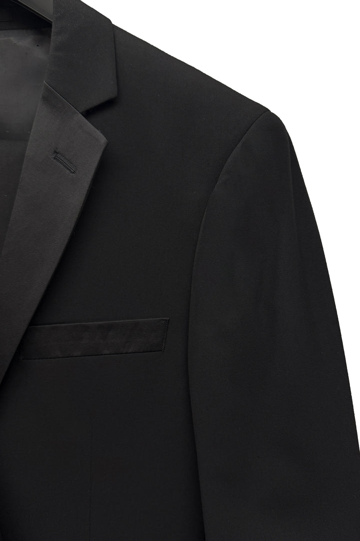 Close-up of the FUBU Classic Notch Lapel Black Tuxedo by Fubu The Colle, slim fit with a notched lapel and breast pocket, shown against a white background.