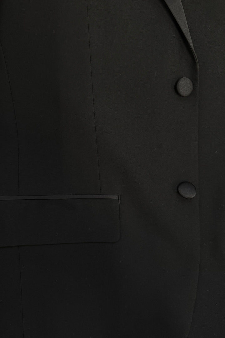 Close-up of the FUBU Classic Notch Lapel Black Tuxedo by Fubu The Colle, featuring a slim fit design with two buttons, part of a pocket, and elegant satin lapels.