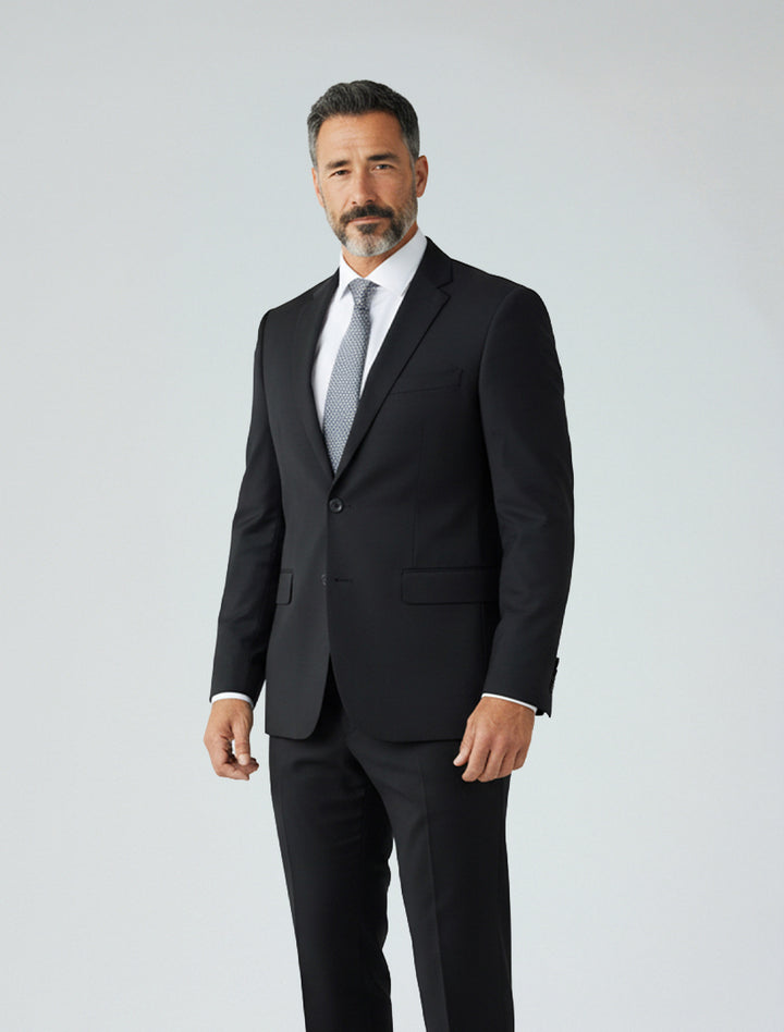 A man with salt-and-pepper hair and a beard is wearing the Karako Men Mens Black Suit with a white shirt and gray tie, standing in front of a plain light background.