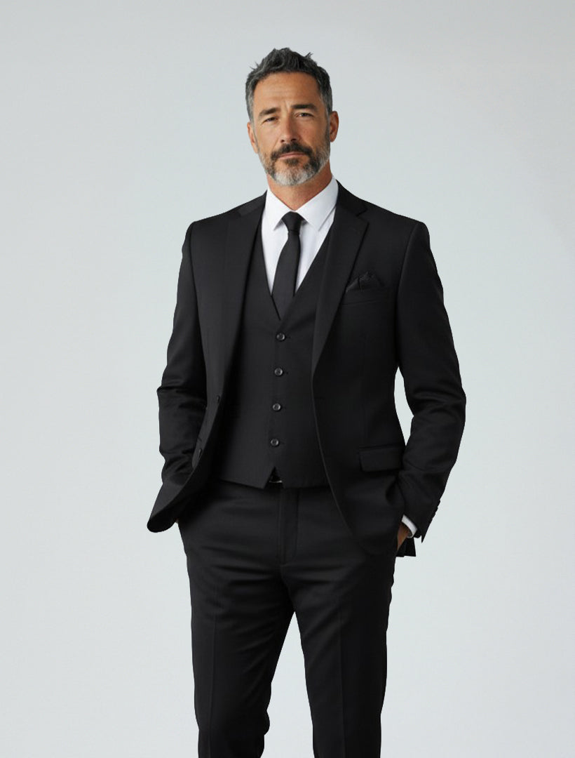 A man with short dark hair and a beard wears the FUBU Black Separates Slim-Fit Jacket by Fubu The Colle over a white shirt and black tie, standing against a plain, light background with his hands in his pockets.