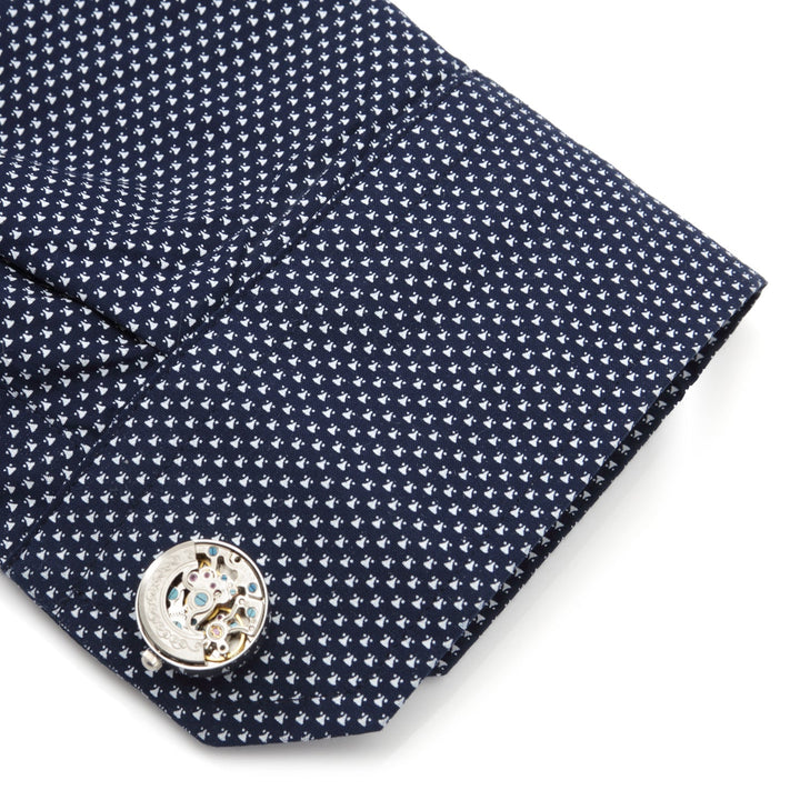A round mechanical watch movement cufflink held by Cufflinks.com Cufflink Adapters on a patterned dark blue dress shirt sleeve.