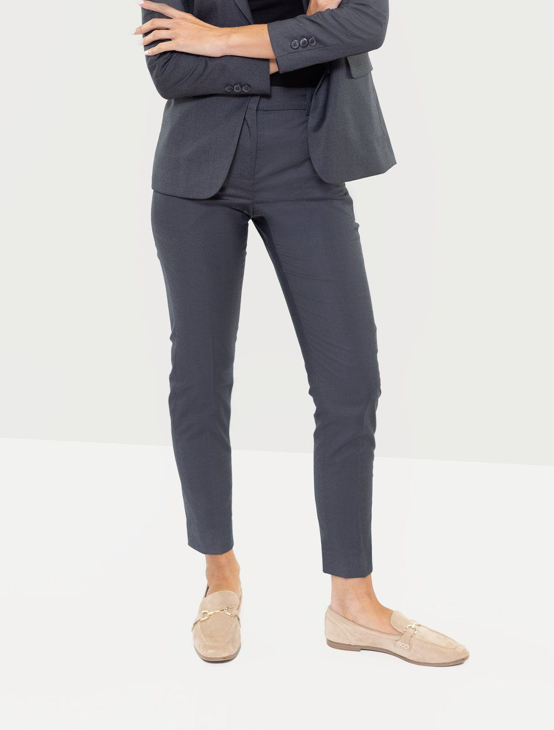 A person wearing Couture 1910 Women's Charcoal Grey Suit Separates Pants and beige loafers stands with arms crossed, their face hidden.