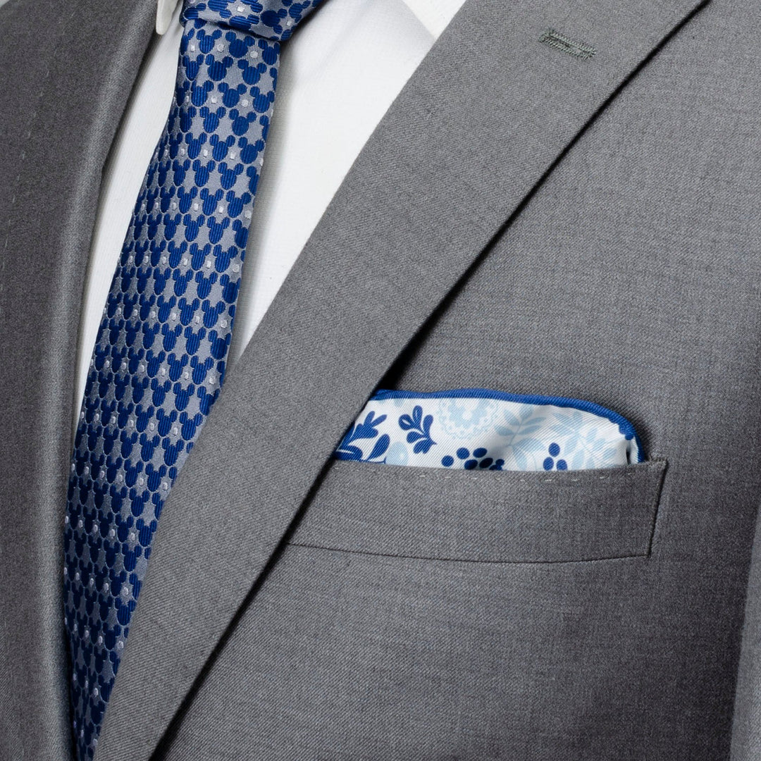 A white silk Disney Mickey Mouse Floral White Pocket Square tucked into a grey suit jacket, paired with a blue tie featuring a repeating Mickey Mouse icon print.