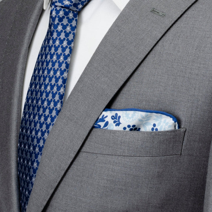 A white silk Disney Mickey Mouse Floral White Pocket Square tucked into a grey suit jacket, paired with a blue tie featuring a repeating Mickey Mouse icon print.