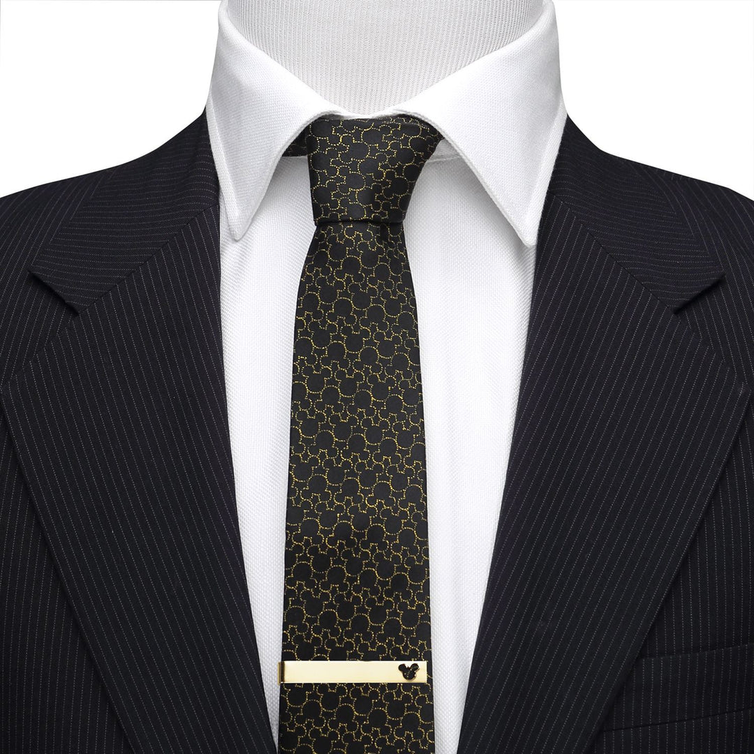 A gold Disney Mickey Mouse Cutout Gold Tie Bar accents a black patterned tie, worn over a white shirt and pinstripe suit jacket.
