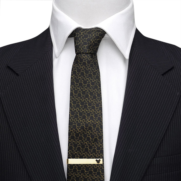 A gold Disney Mickey Mouse Cutout Gold Tie Bar accents a black patterned tie, worn over a white shirt and pinstripe suit jacket.