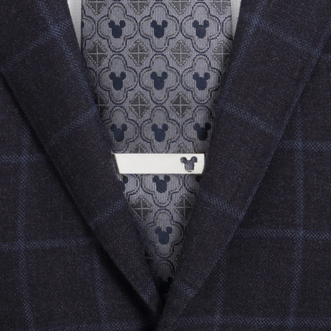 A silver-toned Disney Mickey Mouse Cutout Tie Bar featuring a small cutout, worn over a patterned gray tie and a dark plaid suit jacket.