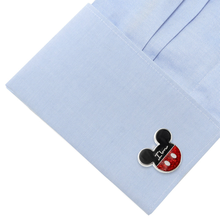 A Disney Mickey and Minnie Mouse “I Love Us” cufflink on a light blue dress shirt cuff, featuring a black top and a sparkly red bottom with the words “I Love” written in white.