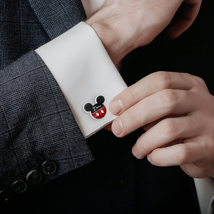 A person wears a white French cuff shirt secured with a Mickey Mouse-shaped Disney Mickey and Minnie Mouse “I Love Us” Cufflink featuring the text “I Love”.