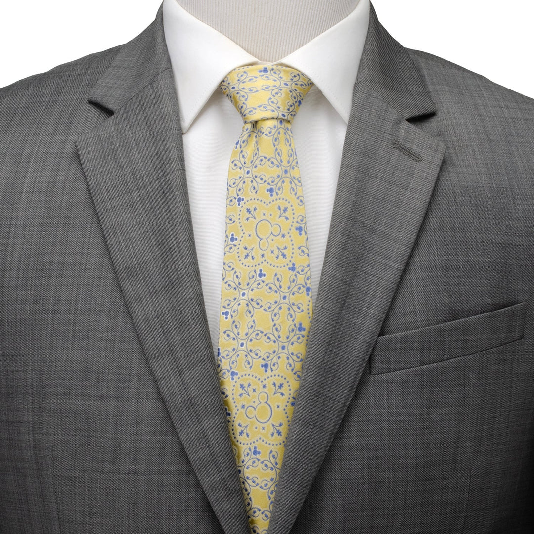 A Disney Mickey Mouse Yellow Multi Men’s Tie with a blue scrolling vine pattern, worn with a white dress shirt and a grey suit jacket.