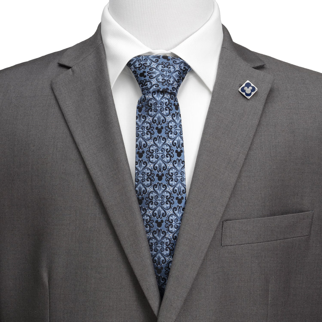 Disney Mickey Mouse Damask Tile Blue Men’s Tie in blue silk with black Mickey Mouse silhouettes, worn with a gray suit, white shirt, and matching square lapel pin.