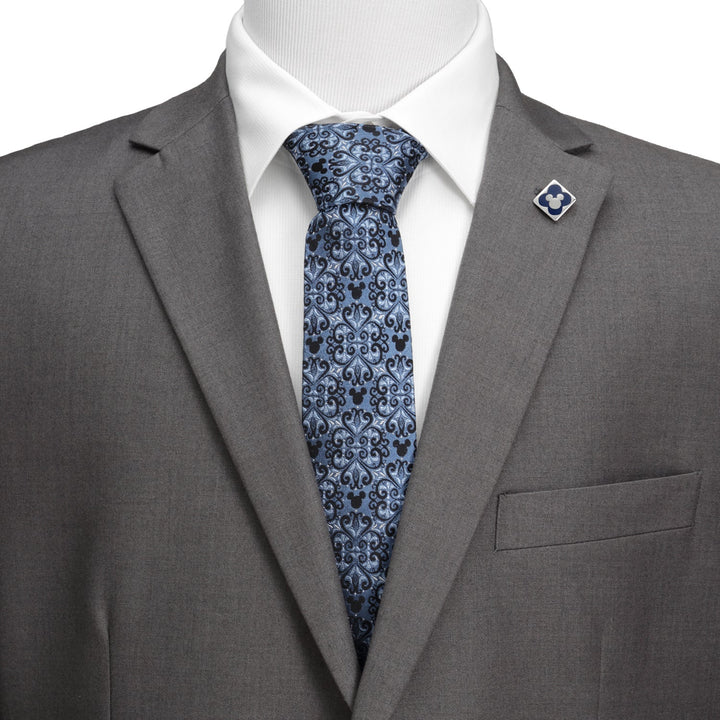 Disney Mickey Mouse Damask Tile Blue Men’s Tie in blue silk with black Mickey Mouse silhouettes, worn with a gray suit, white shirt, and matching square lapel pin.
