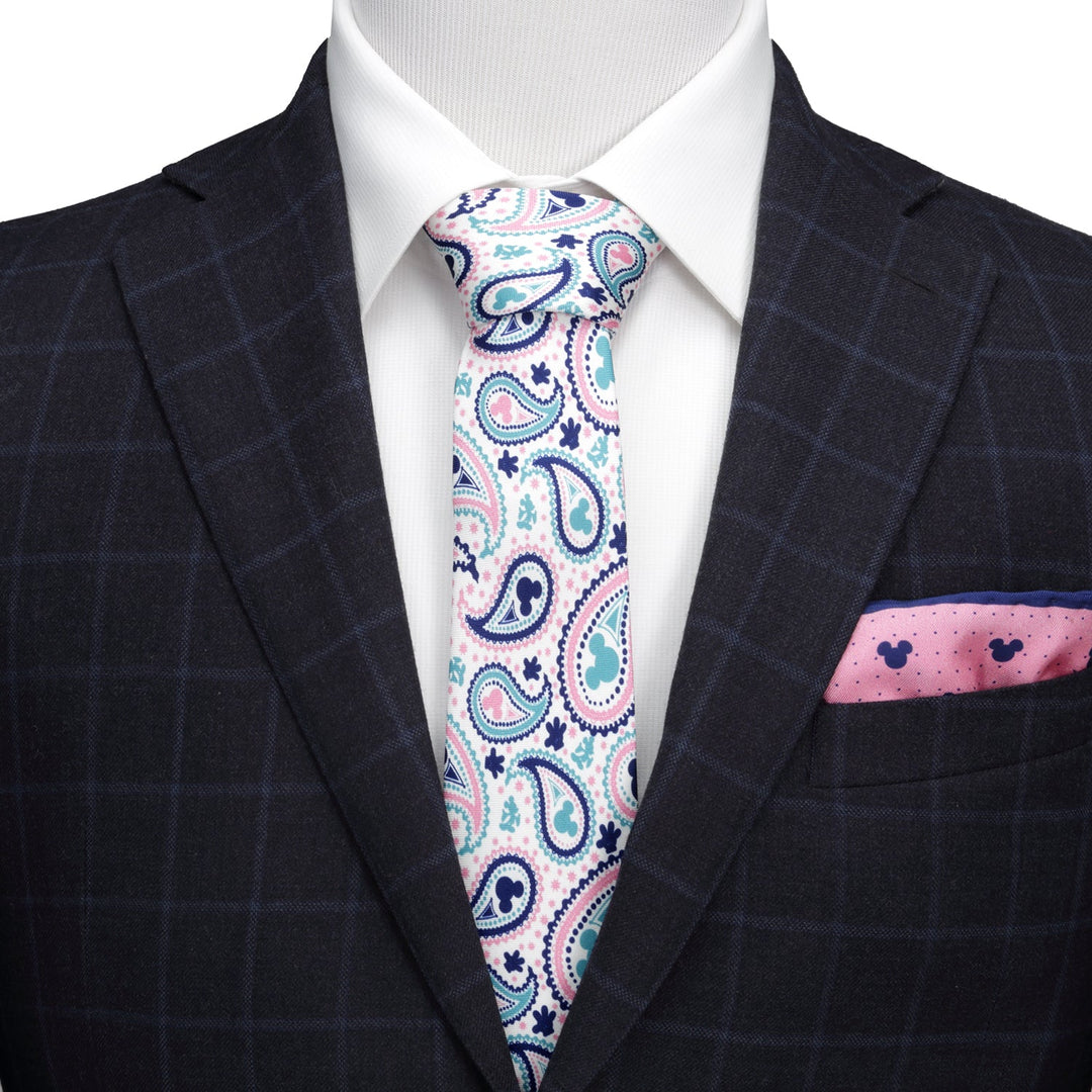 A white Disney Mickey Mouse Paisley Multi Men’s Tie with a pink and blue paisley pattern, worn with a white shirt, a navy windowpane suit jacket, and a matching pink pocket square.