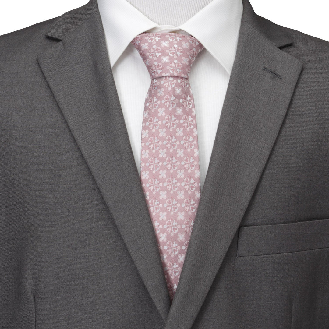 A Disney Mickey Mouse Silhouette Blossom Pink Men’s Tie with a white floral and Mickey Mouse silhouette pattern, worn with a white dress shirt and a grey suit jacket.