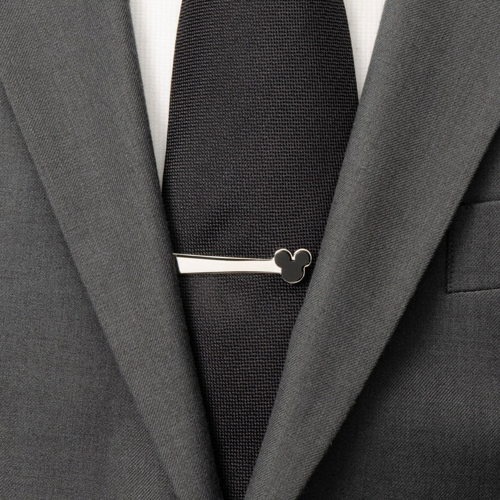 A silver-toned stainless steel Disney Mickey Mouse Onyx Stainless Steel Tie Bar worn on a black tie and grey suit.