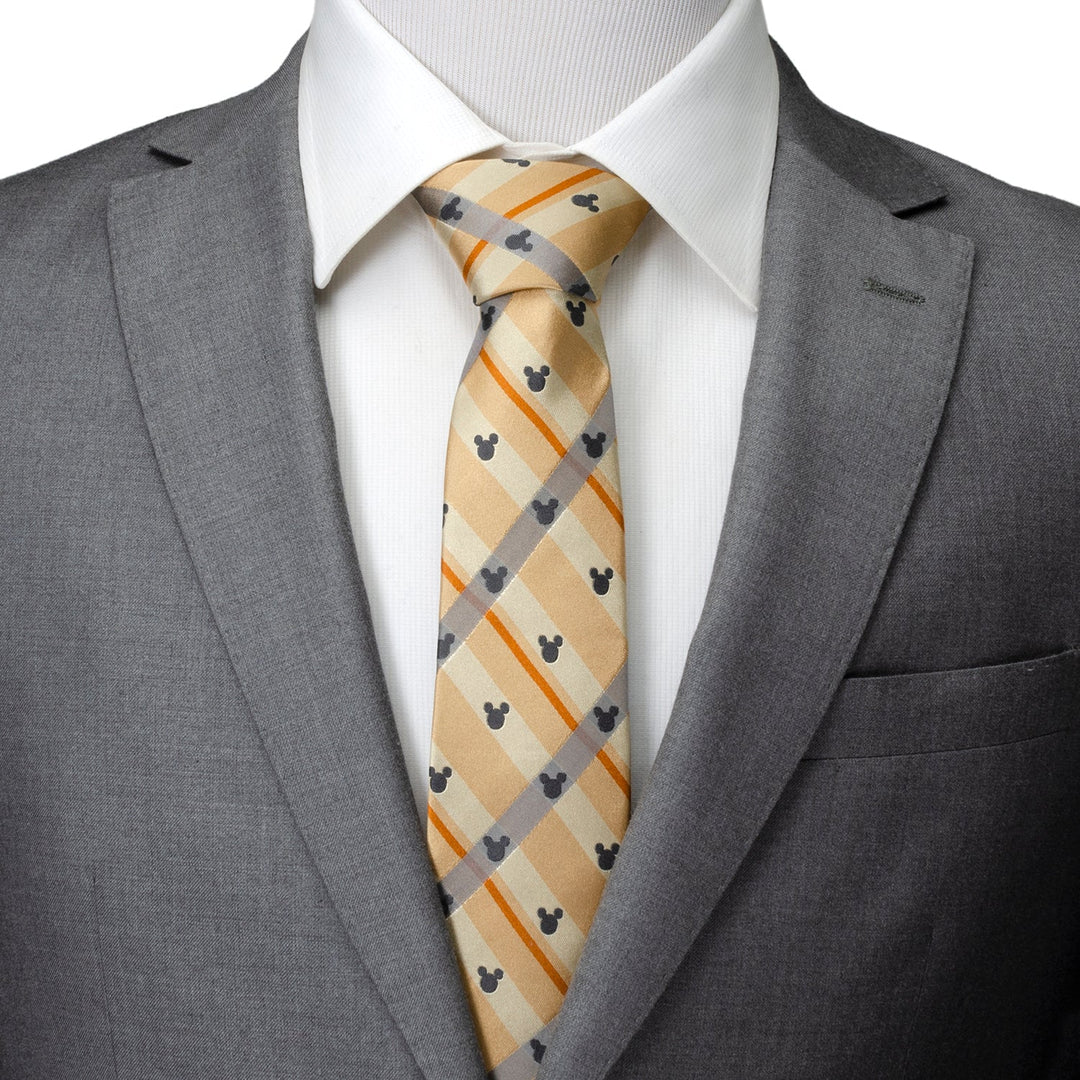 A Disney Mickey Mouse Silhouette Tan Plaid Tie featuring small gray Mickey Mouse silhouettes on tan plaid silk, worn with a white collared shirt and gray suit jacket.