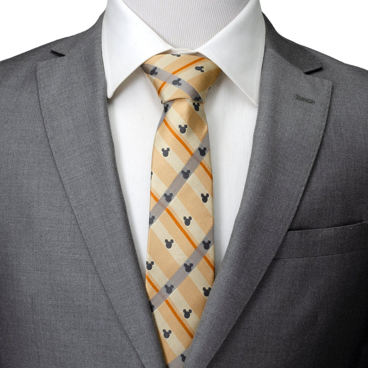 A Disney Mickey Mouse Silhouette Tan Plaid Tie featuring small gray Mickey Mouse silhouettes on tan plaid silk, worn with a white collared shirt and gray suit jacket.