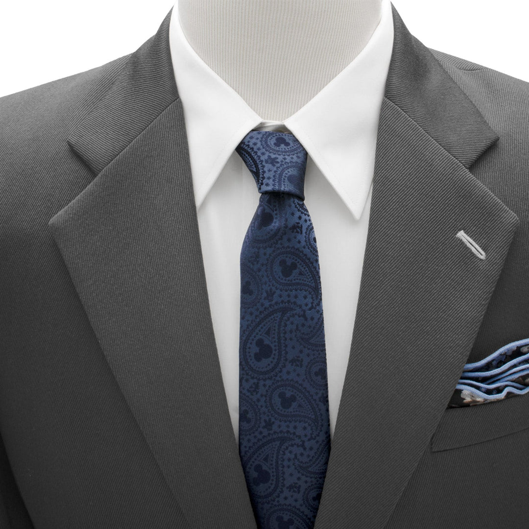 A Disney Mickey Mouse Navy Paisley Men’s Tie in navy blue with a paisley pattern featuring hidden silhouettes, worn with a white dress shirt and a grey suit jacket.