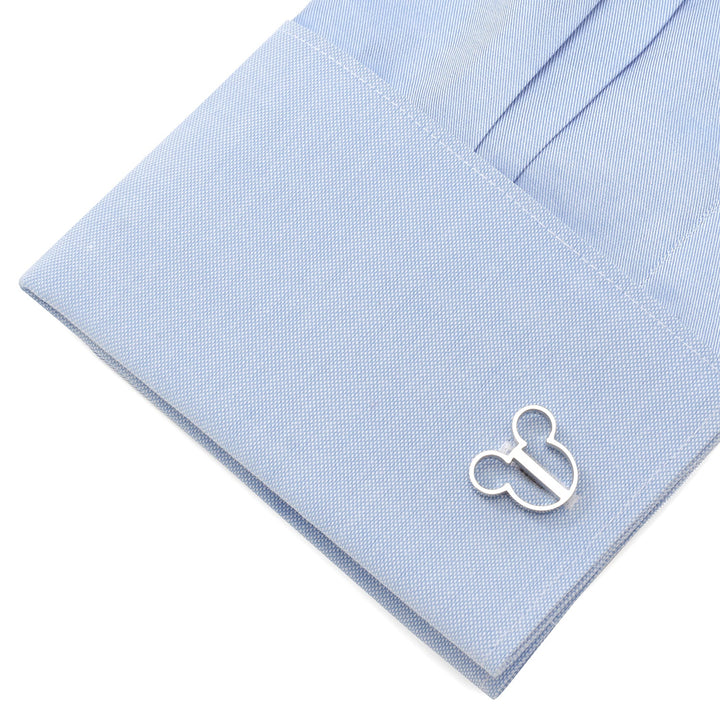 A silver Disney Mickey Mouse Silhouette Cutout Cufflinks piece attached to the cuff of a light blue dress shirt.