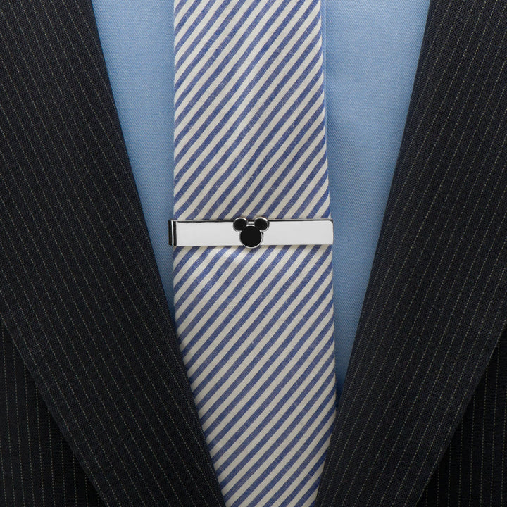 A silver Disney Mickey Mouse Silhouette Tie Bar featuring a black Mickey Mouse silhouette, worn over a blue and white striped tie and a pinstripe suit jacket.