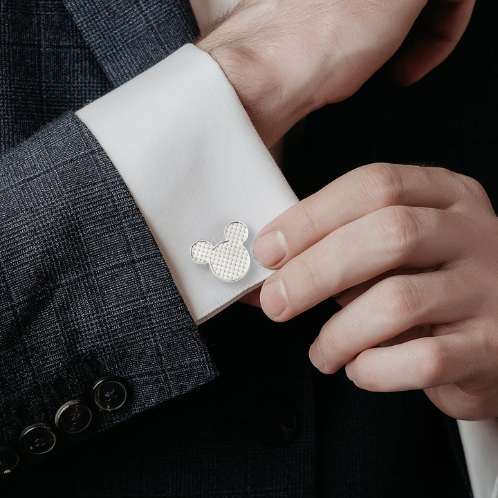 A person in a dark suit adjusts a white shirt sleeve secured with silver Disney Mickey Mouse Silhouette Basket Weave Cufflinks featuring a textured basket weave inlay.
