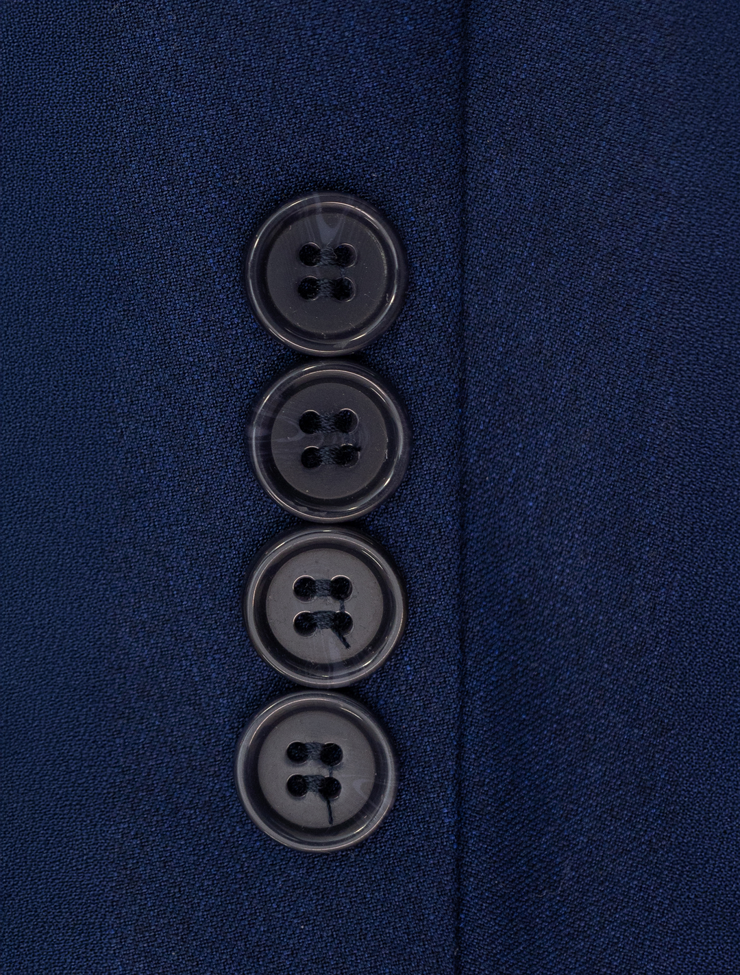 Close-up of four black buttons on the FUBU Indigo Solid Peak Lapel 2-Piece Suit by Fubu The Colle, stitched vertically for a sleek slim fit.