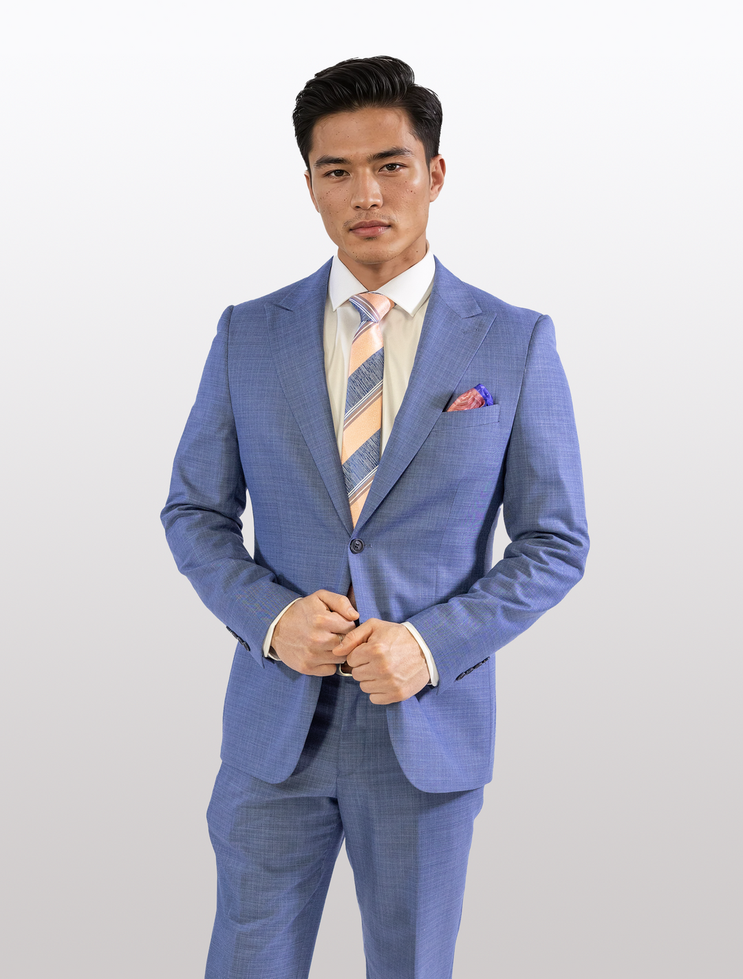 A man wearing a FUBU Stone Blue Peak Lapel 2-Piece Suit from Fubu The Colle stands against a plain background, focusing on the camera as he precisely adjusts his jacket while sporting a striped tie.