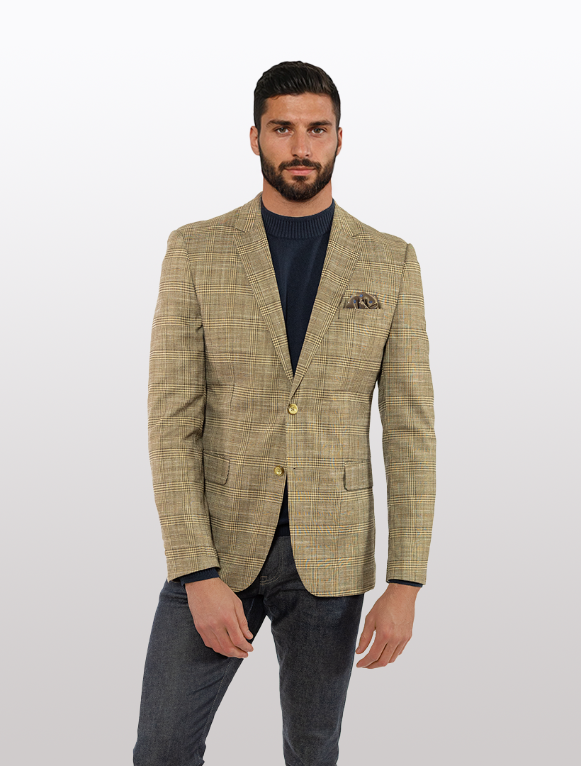 A man wears the FUBU Brown with Tan Tartan Slim Fit Sport Jacket over a navy sweater and jeans, standing poised against a plain background.