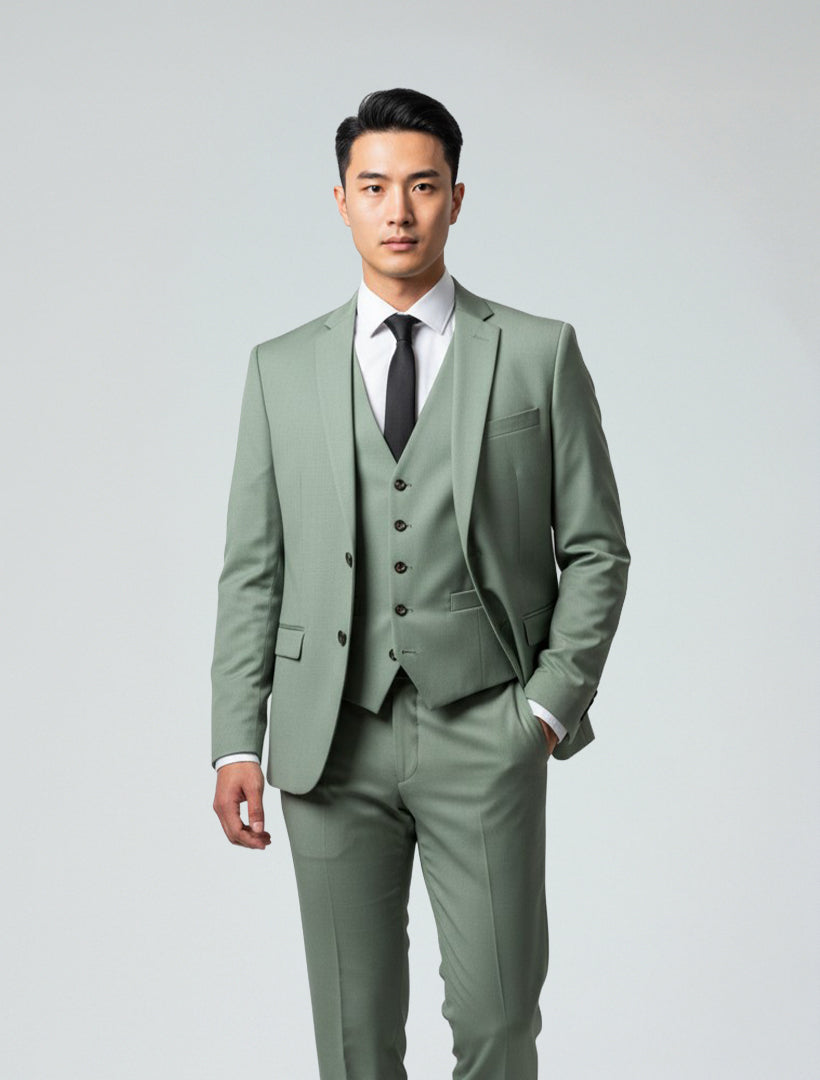 A man wears the Gino Vitale Men's Sage Green Slim Fit Suit, paired with a white shirt and black tie, standing against a plain light gray background.
