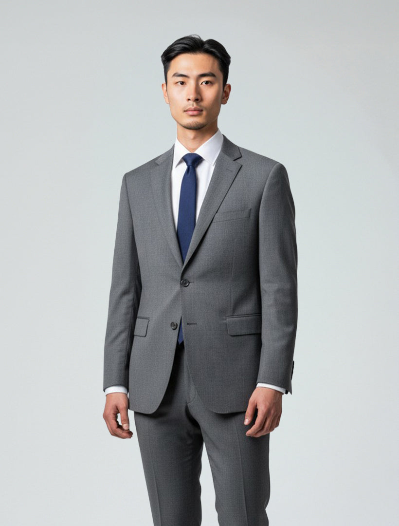 A man wearing the 132 Men's Light Grey Wool Suit, paired with a white dress shirt and navy blue tie, stands facing the camera against a plain light background.