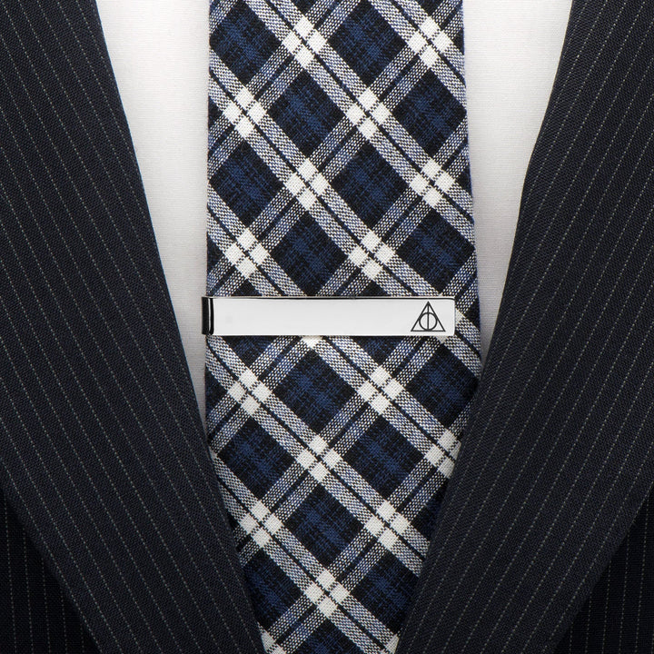A silver Harry Potter Deathly Hallows “Always” Hidden Message Tie Bar clipped to a blue, black, and white plaid tie worn with a pinstripe suit jacket.