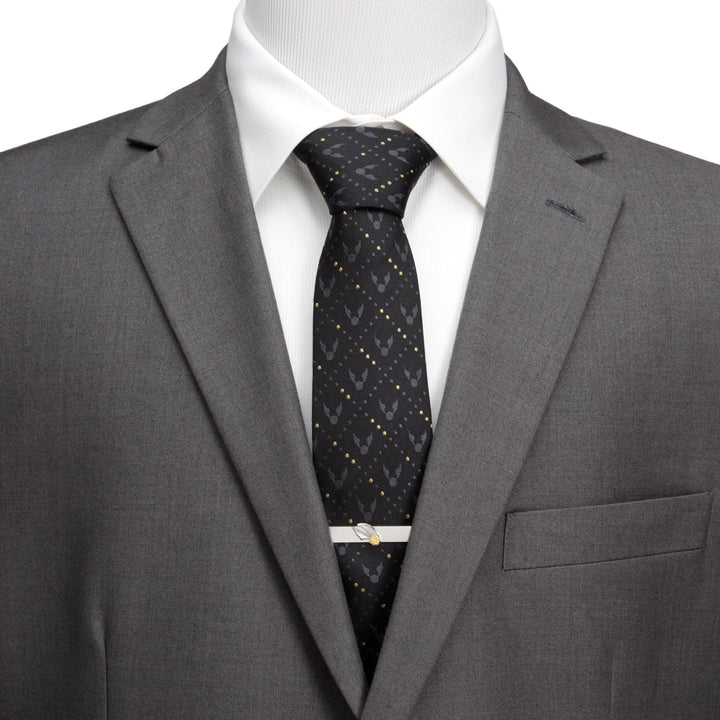 A Harry Potter Golden Snitch Black Silk Men’s Tie patterned with golden snitches and secured by a silver snitch tie clip, worn with a white shirt and gray suit jacket.