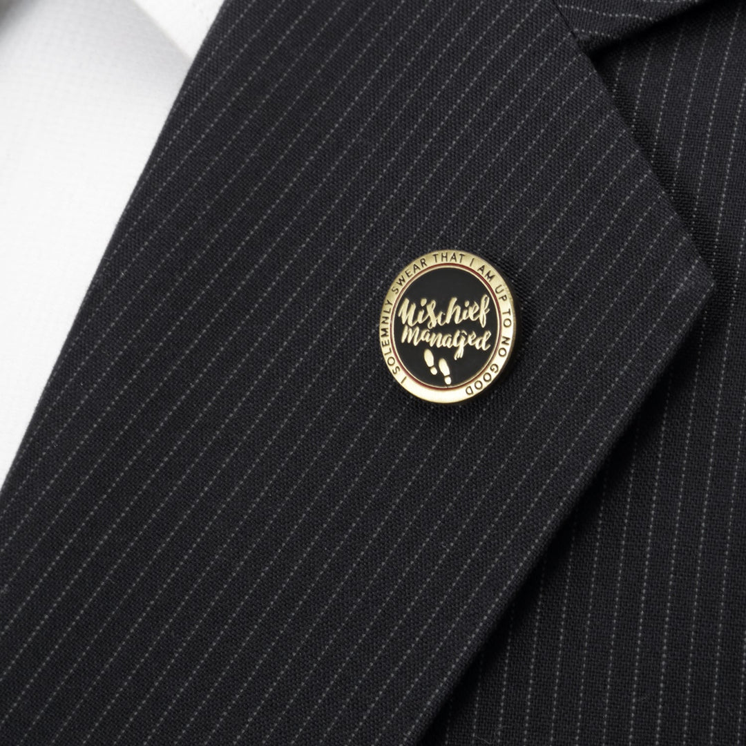 Harry Potter Mischief Managed Gold Lapel Pin, a round black and gold pin with footprints attached to a pinstripe suit lapel.