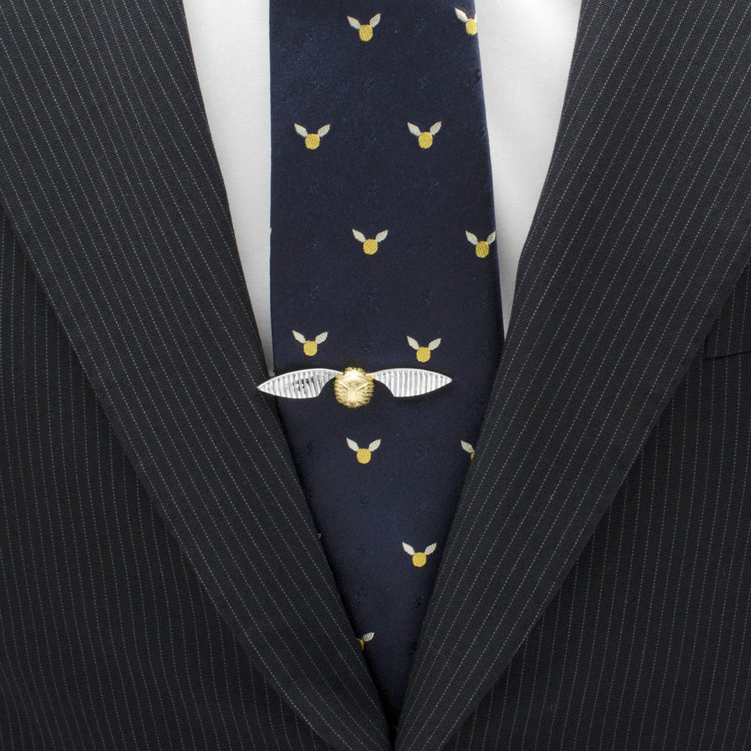 A Harry Potter Golden Snitch Tie Clip secured on a dark patterned tie worn with a pinstripe suit jacket and white shirt.