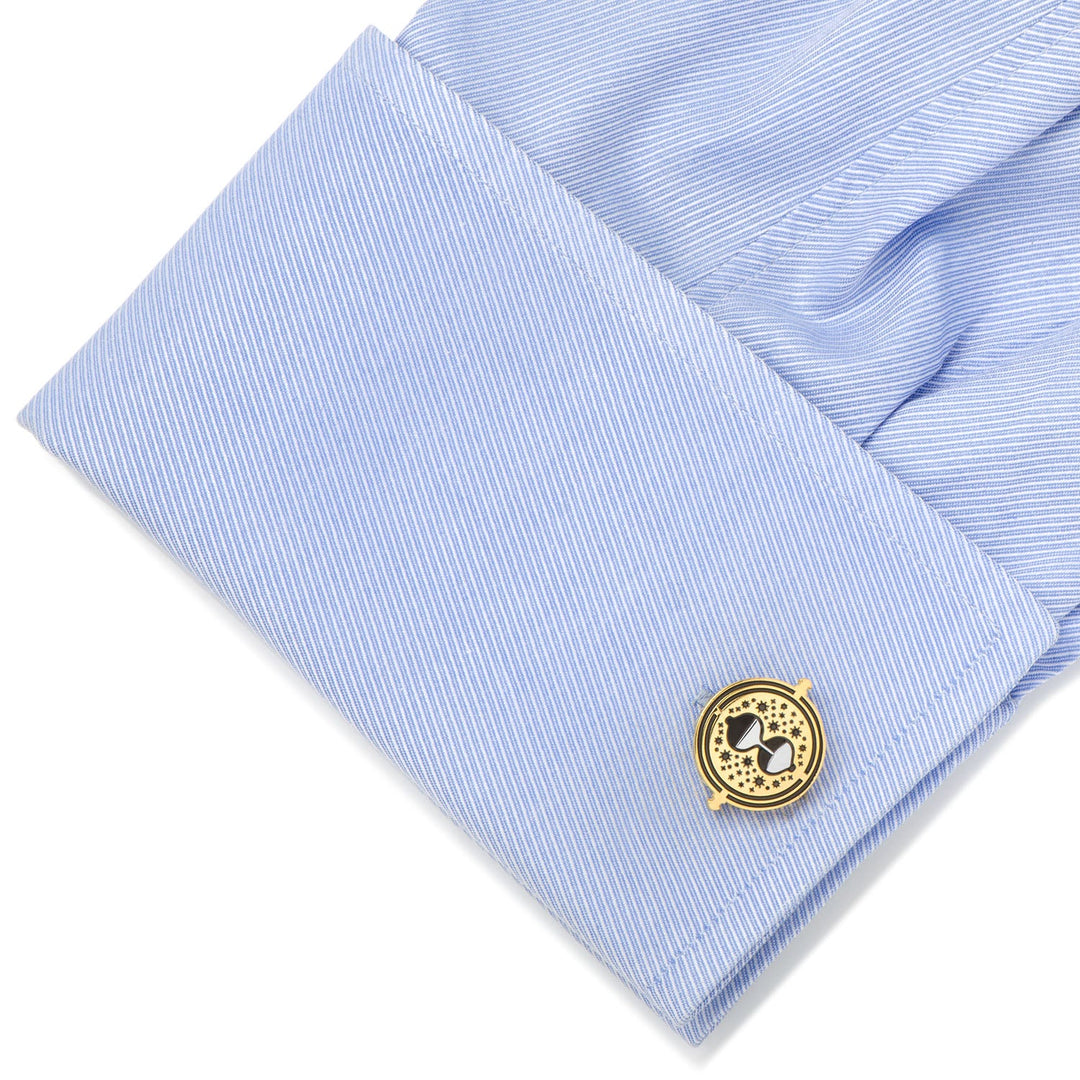Gold-colored Harry Potter Hermione’s Time Turner cufflinks with an hourglass design on a light blue dress shirt cuff.