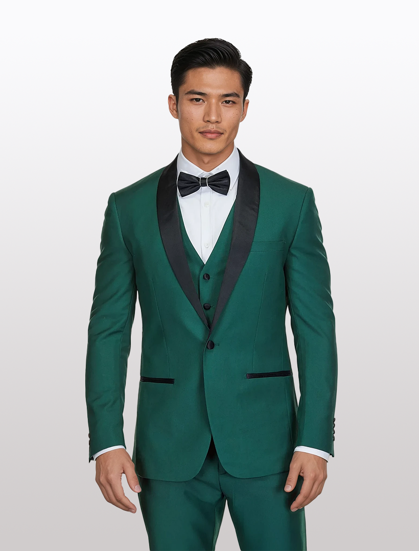 A man in a Gino Vitale Men's Hunter Green Shawl Lapel Tailored Fit Tuxedo, designed with Tetron Rayon and featuring a black bow tie and lapel, stands poised against a light background.