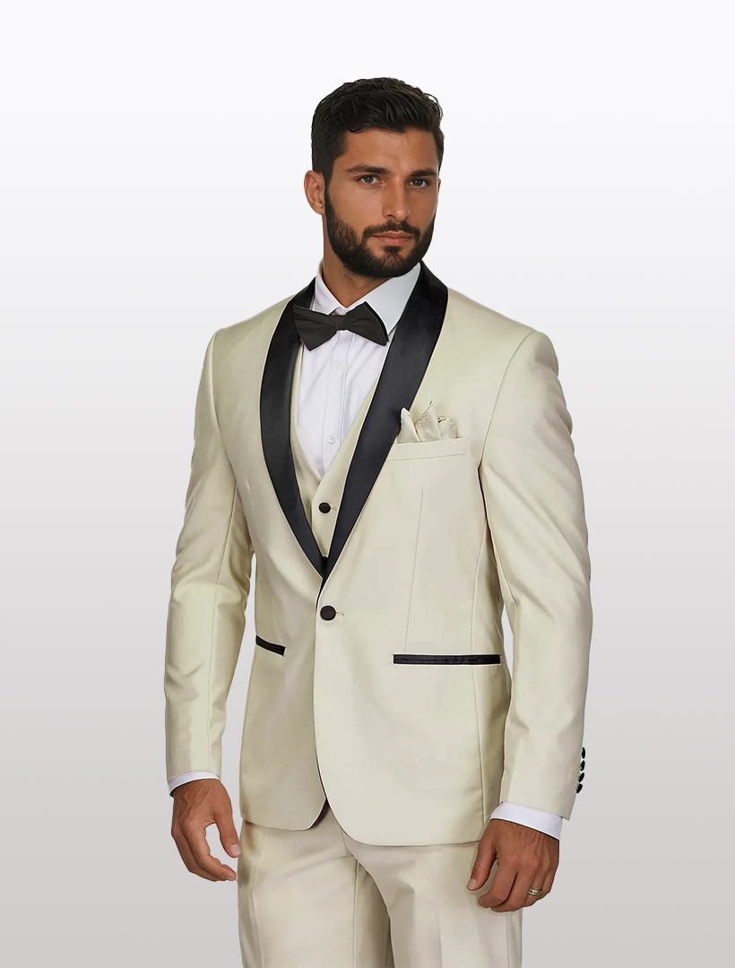 A man wears a Gino Vitale Men's Ivory Shawl Lapel Tailored Fit Tuxedo, featuring black lapels and a bow tie, against a plain background. Crafted in Tetron Rayon, it blends elegance with modern sophistication.