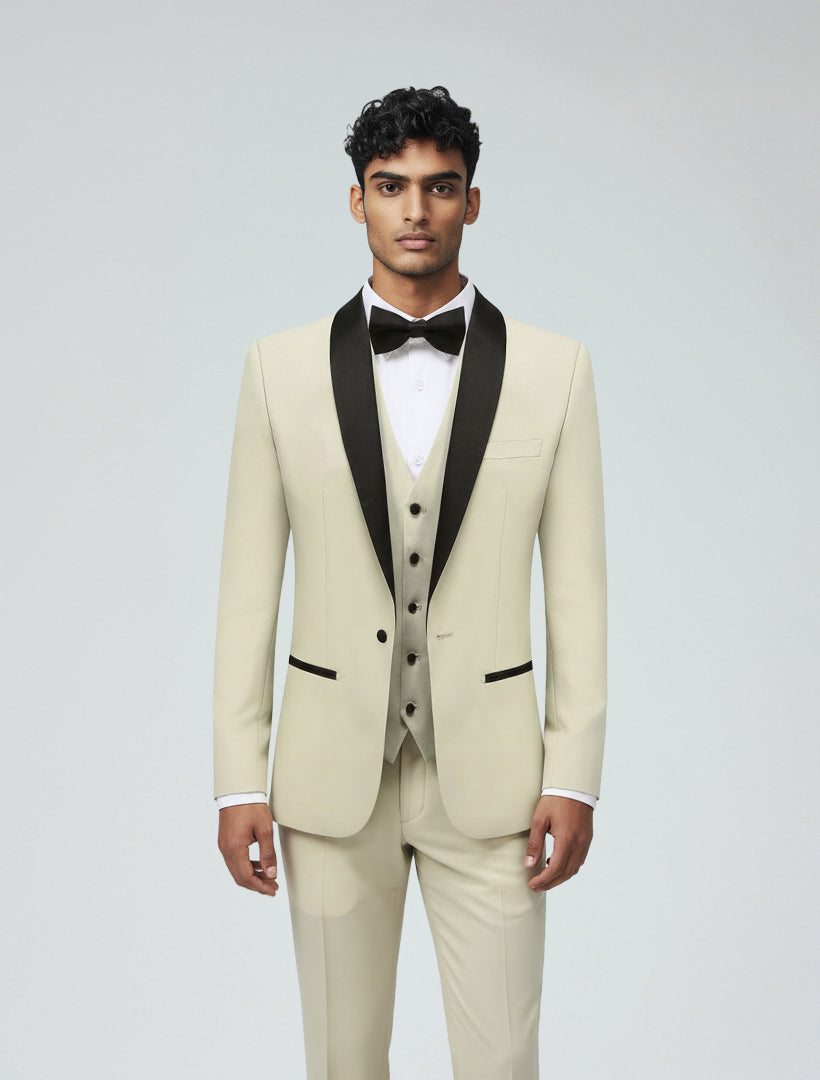 A man faces forward in a Gino Vitale Men's Ivory Shawl Lapel Tailored Fit Tuxedo, featuring a satin shawl lapel, white dress shirt, black bow tie, and beige waistcoat.